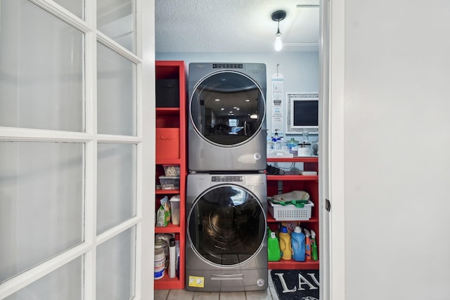 clothes washing area featuring a textured ceiling, stacked washer / dryer, and tile patterned floors