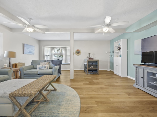 living room featuring light wood-type flooring, ceiling fan, a textured ceiling, and baseboards