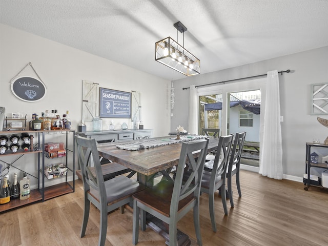 dining space featuring a chandelier, a textured ceiling, baseboards, and wood finished floors