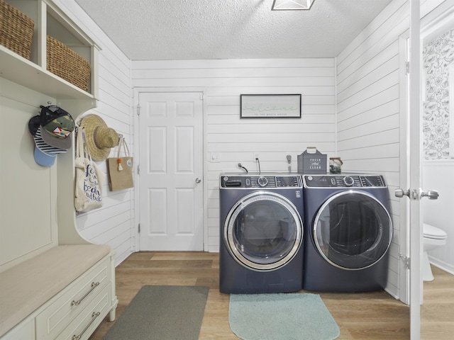 laundry room featuring a textured ceiling, light hardwood / wood-style flooring, wood walls, and independent washer and dryer