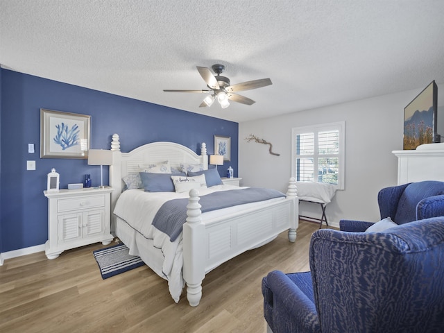 bedroom featuring ceiling fan, a textured ceiling, baseboards, and wood finished floors