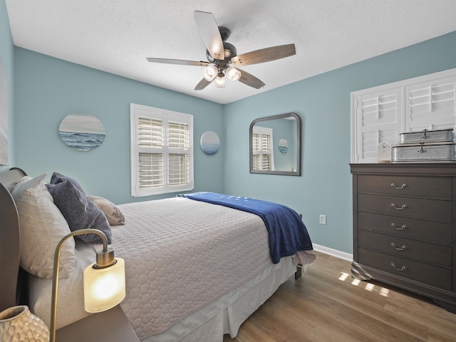 bedroom with a textured ceiling, ceiling fan, wood finished floors, and baseboards