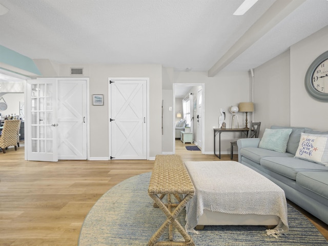 living area featuring a textured ceiling, light wood-type flooring, visible vents, and baseboards