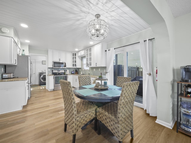 dining room with a notable chandelier, light hardwood / wood-style floors, wood ceiling, washer / clothes dryer, and sink