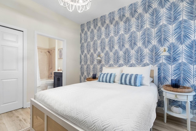 bedroom featuring light wood-type flooring, connected bathroom, and an inviting chandelier