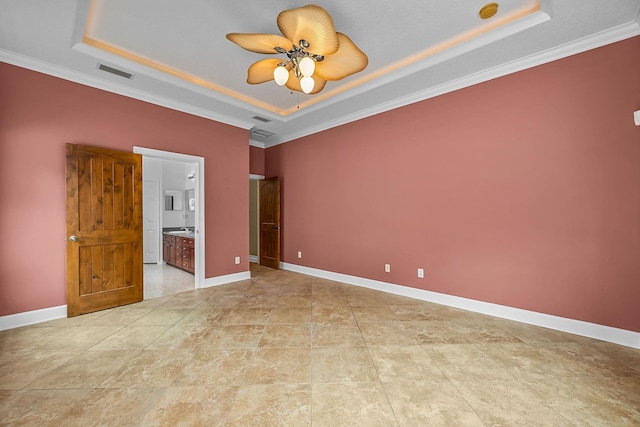 unfurnished bedroom featuring a tray ceiling, ensuite bath, ceiling fan, and ornamental molding