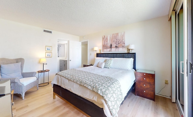 bedroom featuring a textured ceiling, light wood-type flooring, and ensuite bathroom