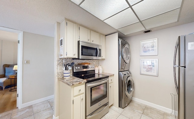 kitchen with decorative backsplash, light tile patterned flooring, stacked washer / dryer, and stainless steel appliances