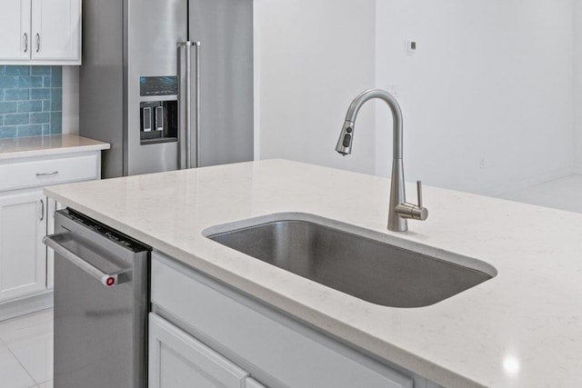 kitchen featuring white cabinetry, decorative backsplash, a sink, appliances with stainless steel finishes, and light stone countertops