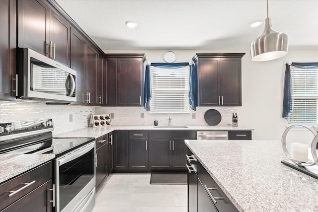 kitchen with dark brown cabinetry, sink, stainless steel appliances, tasteful backsplash, and decorative light fixtures