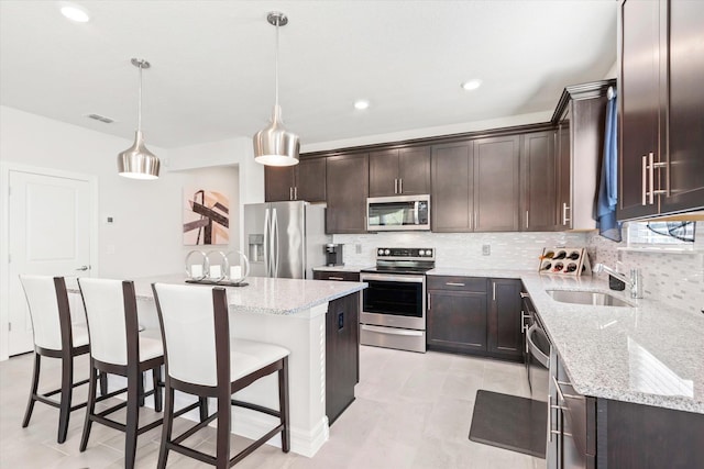 kitchen with backsplash, stainless steel appliances, sink, a kitchen island, and hanging light fixtures