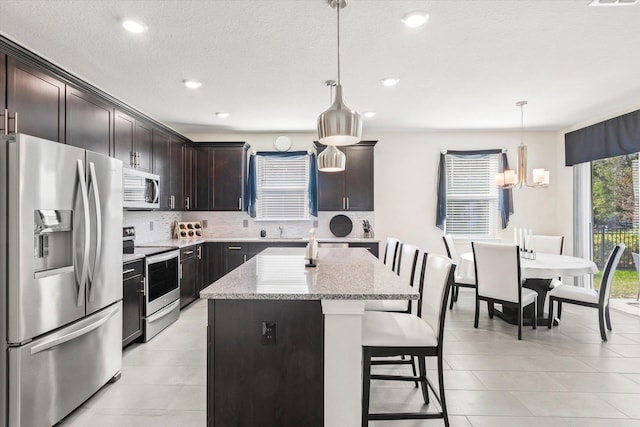 kitchen featuring dark brown cabinetry, stainless steel appliances, a notable chandelier, pendant lighting, and a kitchen island