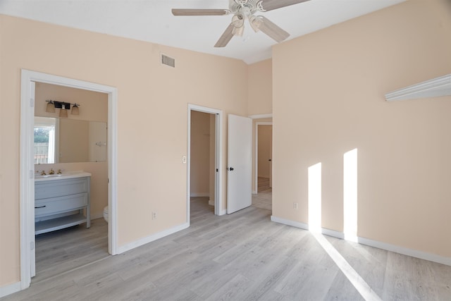 unfurnished bedroom featuring ensuite bathroom, a spacious closet, light wood-type flooring, a closet, and ceiling fan