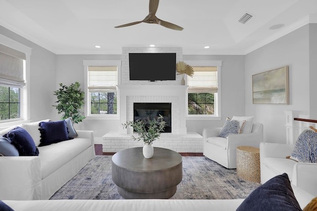 living area with visible vents, a tray ceiling, recessed lighting, crown molding, and a brick fireplace