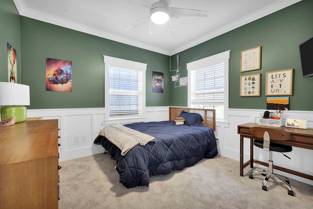 carpeted bedroom with wainscoting, ceiling fan, and ornamental molding