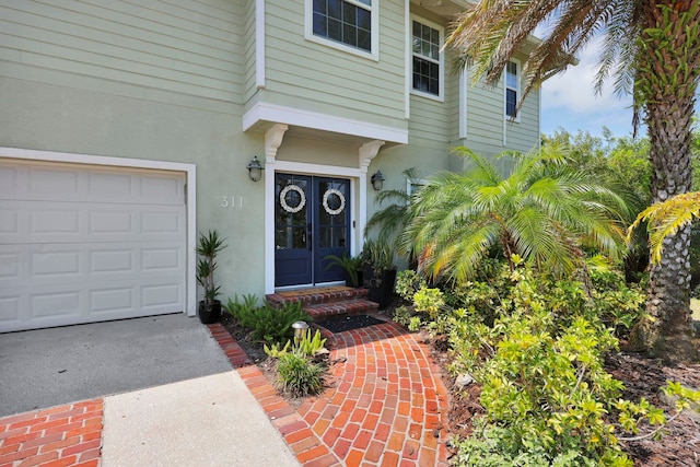 doorway to property featuring stucco siding, french doors, concrete driveway, and a garage