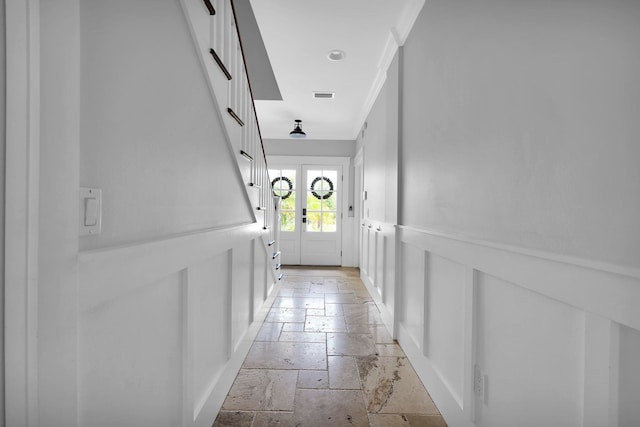 hall with stone tile floors, visible vents, french doors, and ornamental molding