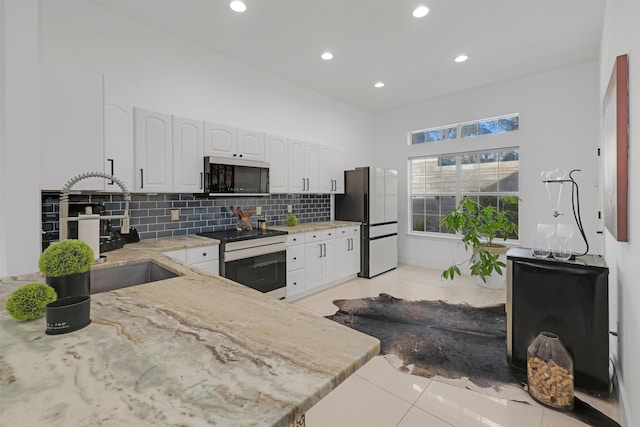 kitchen featuring sink, light tile patterned floors, refrigerator, white cabinetry, and stainless steel electric stove