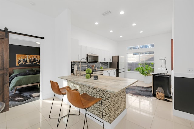 kitchen with refrigerator, white cabinetry, a kitchen bar, kitchen peninsula, and a barn door