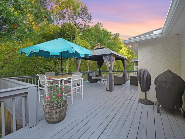 deck at dusk with a gazebo, grilling area, outdoor dining area, and an outdoor living space