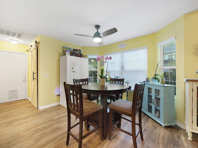 dining room featuring a barn door, light wood-type flooring, baseboards, visible vents, and a ceiling fan