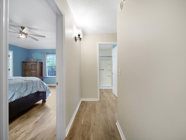 hall with light wood-style floors, a textured ceiling, and baseboards