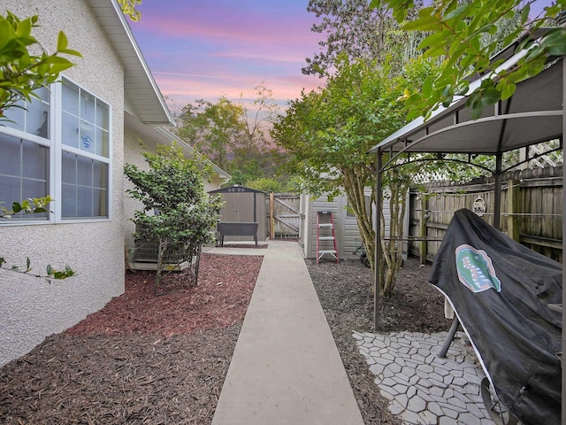 yard at dusk featuring a gate, a gazebo, a patio area, and a fenced backyard