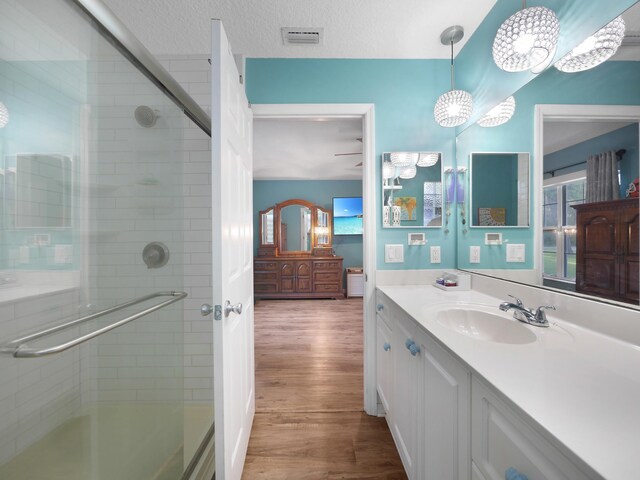 full bathroom featuring a shower with shower door, wood finished floors, visible vents, and vanity