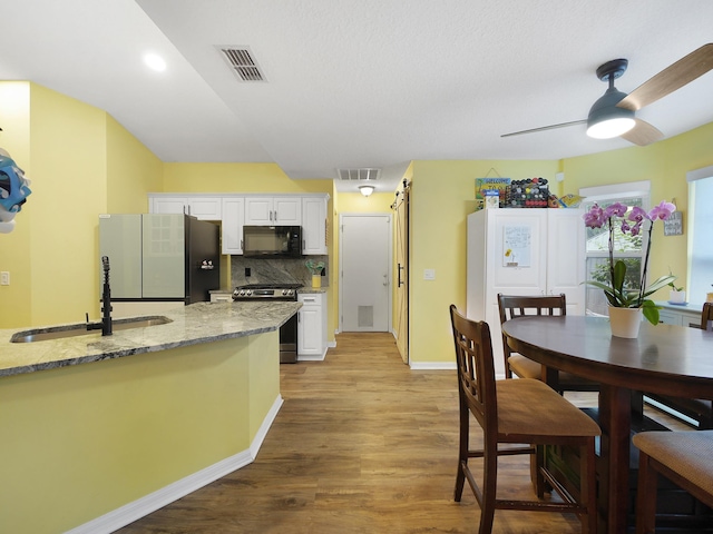 kitchen with electric stove, a sink, black microwave, light wood-style flooring, and freestanding refrigerator