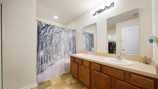 bathroom with a textured ceiling, double vanity, shower / bath combo, and a sink