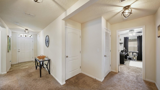 hallway featuring light carpet, visible vents, baseboards, and a textured ceiling