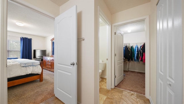 bedroom featuring a closet, a spacious closet, light carpet, a textured ceiling, and baseboards