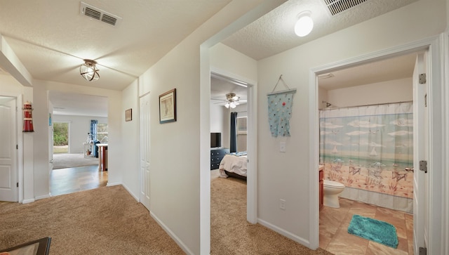 hallway featuring light carpet, a textured ceiling, visible vents, and baseboards