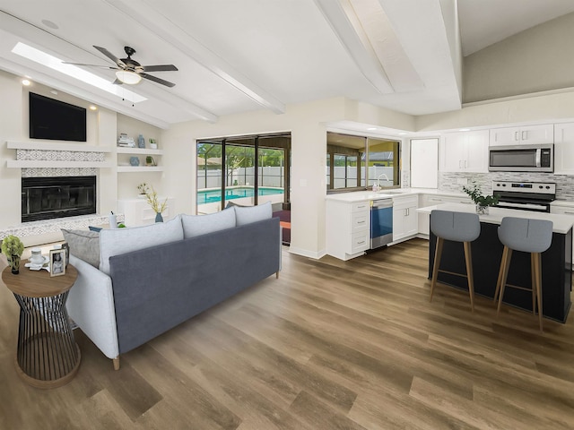 living room with vaulted ceiling with beams, ceiling fan, sink, and dark hardwood / wood-style flooring