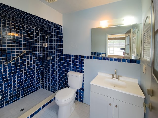 bathroom featuring a tile shower, tile patterned floors, toilet, vanity, and tile walls