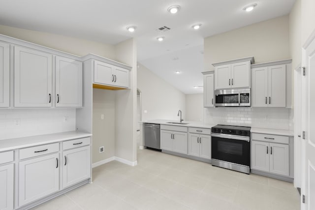 kitchen with sink, light tile patterned floors, stainless steel appliances, decorative backsplash, and vaulted ceiling