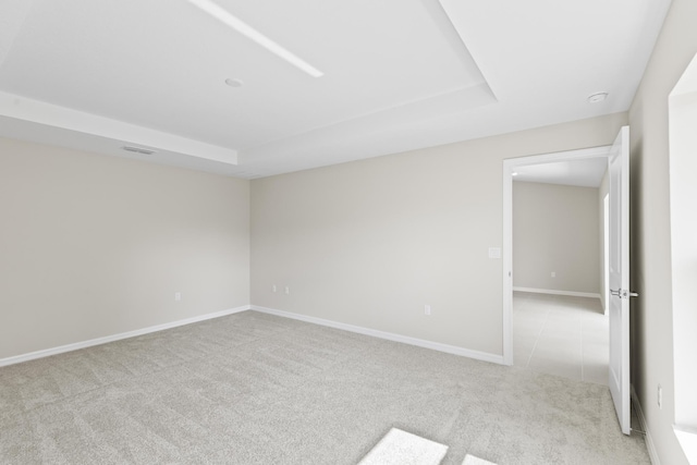 spare room with a tray ceiling and light carpet