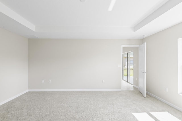 empty room with a raised ceiling and light carpet