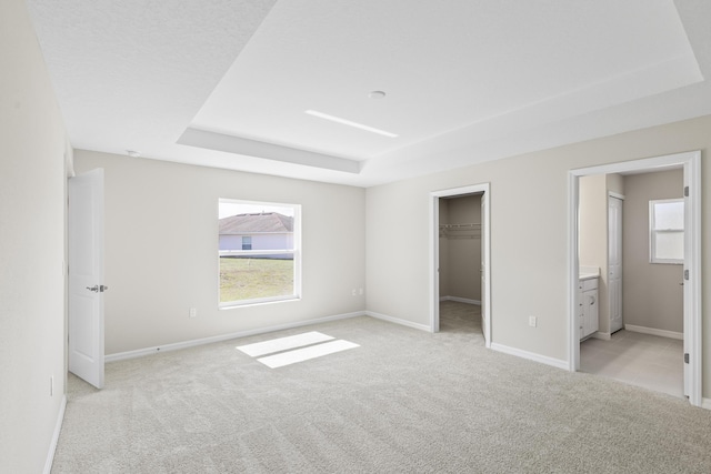 unfurnished bedroom featuring a walk in closet, ensuite bath, light carpet, a raised ceiling, and a closet