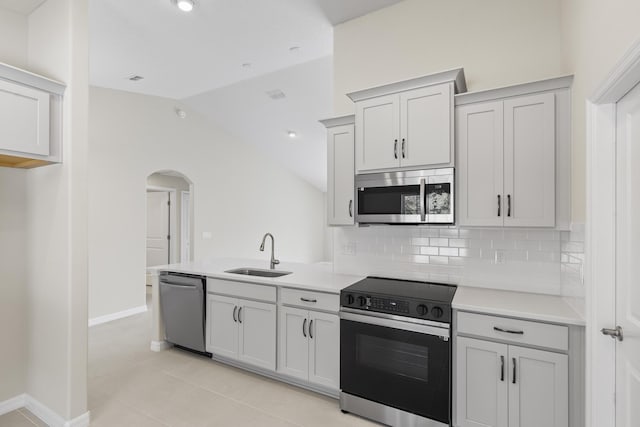 kitchen featuring sink, light tile patterned floors, appliances with stainless steel finishes, tasteful backsplash, and vaulted ceiling