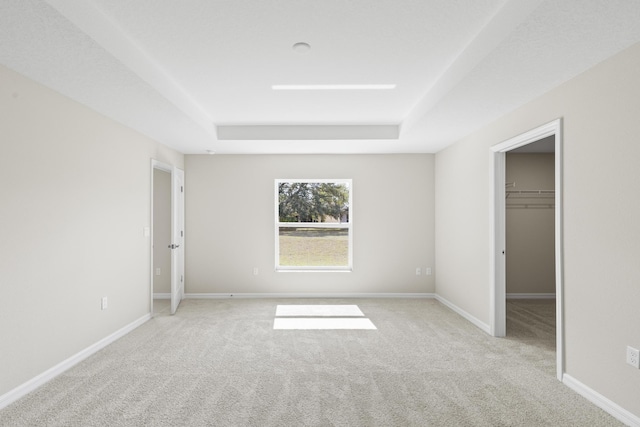 unfurnished bedroom with a walk in closet, light colored carpet, and a tray ceiling