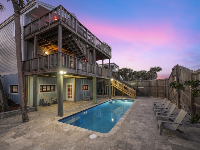 pool at dusk with a wooden deck and a patio