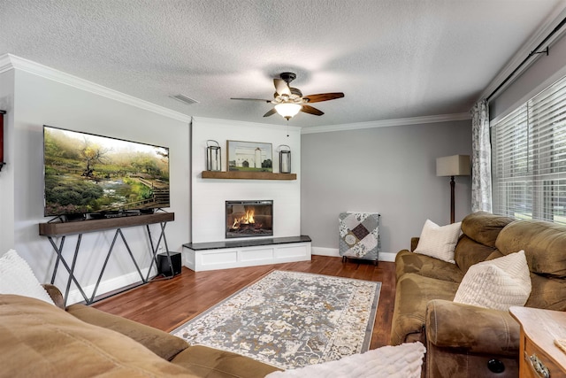 living room with ceiling fan, dark wood-type flooring, a textured ceiling, and ornamental molding