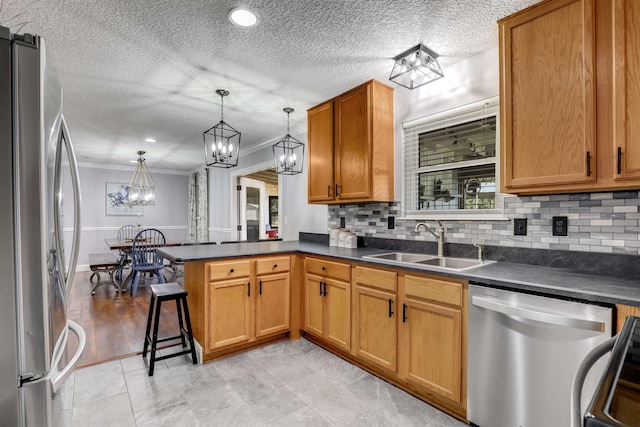 kitchen with sink, kitchen peninsula, crown molding, decorative light fixtures, and appliances with stainless steel finishes