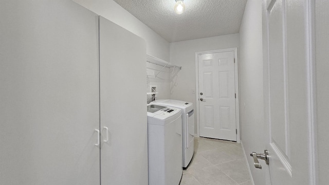 clothes washing area featuring washer and dryer, a textured ceiling, and light tile patterned flooring