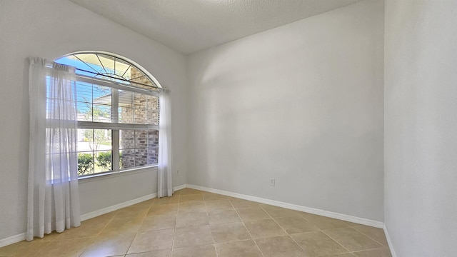spare room featuring light tile patterned flooring, baseboards, and a textured ceiling