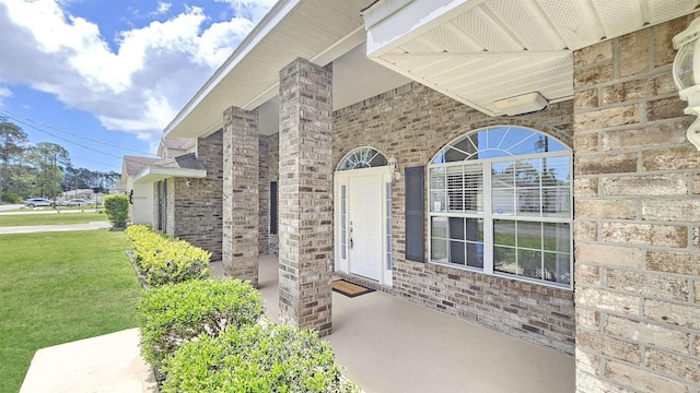 view of exterior entry with brick siding and a lawn