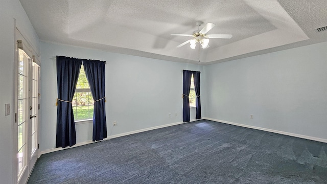 unfurnished room with a textured ceiling, a tray ceiling, dark carpet, ceiling fan, and baseboards