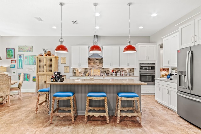 kitchen with decorative light fixtures, stainless steel appliances, a kitchen island with sink, and a breakfast bar area