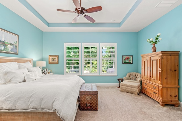 bedroom with a raised ceiling, ceiling fan, and light colored carpet